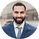 Man in suit smiling outdoors, urban background.
